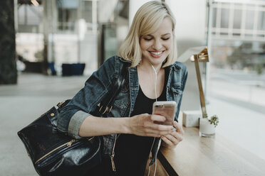 Happy woman using mobile phone while standing by table at cafe - CAVF58125