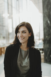 Smiling woman looking away while standing in cafe - CAVF58135