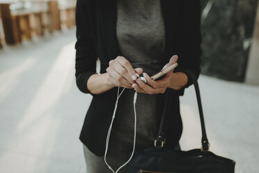 Mittelteil einer Frau, die in einem Café stehend ihr Handy und ihre Handtasche hält - CAVF58136