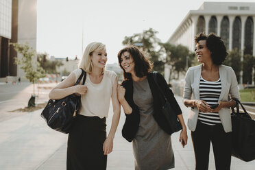 Happy friends talking while walking on city street against sky - CAVF58142