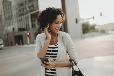 Happy woman listening music while standing on city street - CAVF58145