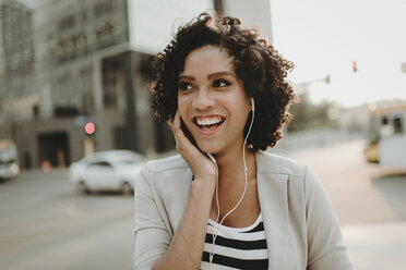 Happy woman looking away while listening music on city street - CAVF58146