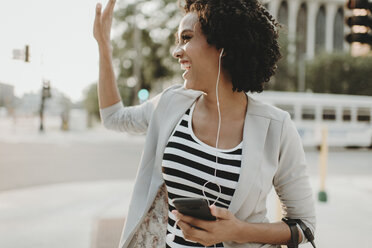 Happy woman waving while listening music on city street - CAVF58147