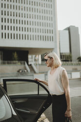 Lächelnde Frau, die eine Autotür hält, während sie an einem Gebäude in der Stadt steht - CAVF58149