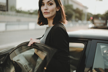 Portrait of confident woman boarding into car in city - CAVF58150