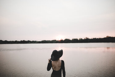 Rückansicht einer Frau, die einen Hut trägt, während sie am See vor dem Himmel steht - CAVF58164