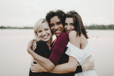 Portrait of cheerful female friends embracing against lake - CAVF58166