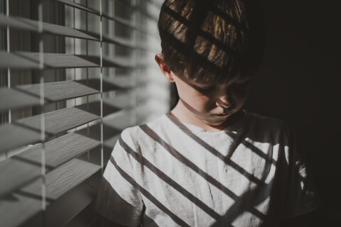 Junge steht am Fenster zu Hause, lizenzfreies Stockfoto