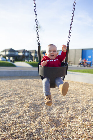 Süßes Baby Junge schwingt gegen den Himmel im Park, lizenzfreies Stockfoto