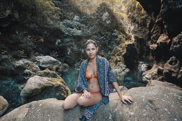 Portrait of woman wearing bikini with scarf sitting on rock - CAVF58234