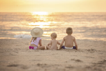 Rückansicht von Geschwistern, die bei Sonnenuntergang am Strand sitzen - CAVF58264