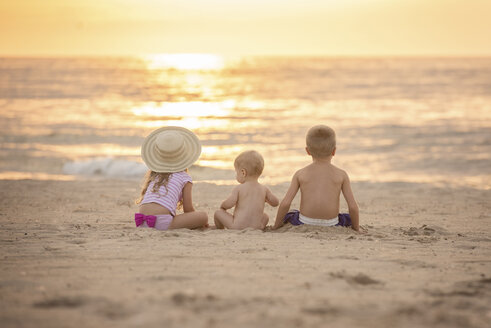 Rückansicht von Geschwistern, die bei Sonnenuntergang am Strand sitzen - CAVF58264