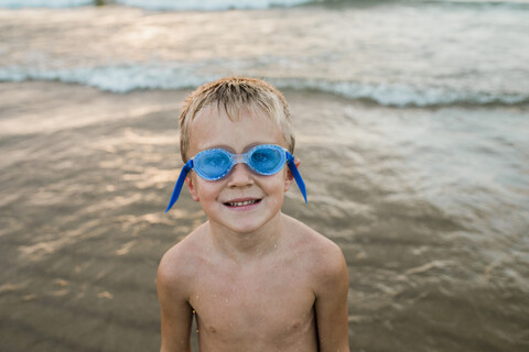 Porträt eines Jungen ohne Hemd, der eine Schwimmbrille trägt, während er am Ufer des Strandes steht, lizenzfreies Stockfoto