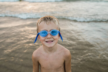 Porträt eines Jungen ohne Hemd, der eine Schwimmbrille trägt, während er am Ufer des Strandes steht - CAVF58266