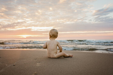 In voller Länge von nackten Baby Junge sitzt auf Sand am Strand gegen bewölkten Himmel bei Sonnenuntergang - CAVF58267