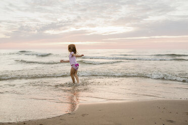 Carefree girl playing on shore at beach against cloudy sky during sunset - CAVF58268