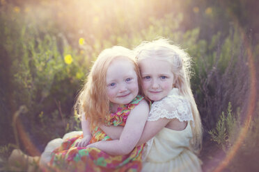 Portrait of cute sisters sitting on field during sunny day - CAVF58276