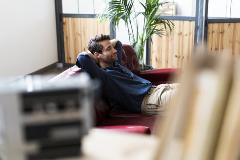 Young man sitting on couch with closed eyes - GIOF04957