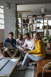 Business team using laptop and discussing documents in loft office - GIOF04985