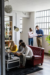 Business team using laptop and discussing documents in loft office - GIOF04992