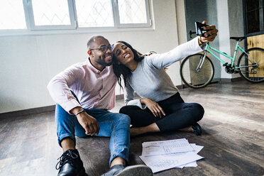 Smiling businessman and businesswoman sitting on the floor taking a selfie - GIOF05029