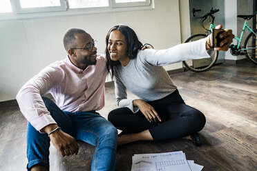 Smiling businessman and businesswoman sitting on the floor taking a selfie - GIOF05030