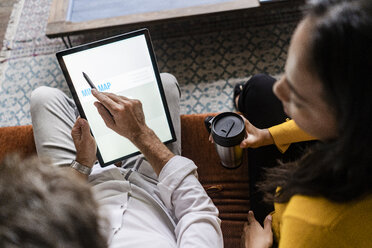Geschäftsfrau und Geschäftsmann teilen sich ein Tablet auf einem Sofa in einem Loft-Büro - GIOF05041