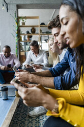 Business team sitting in loft office using cell phones - GIOF05049