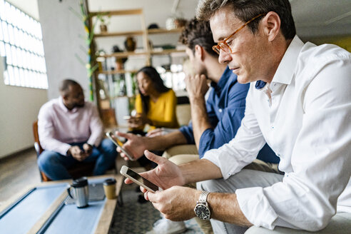 Business team sitting in loft office using cell phones - GIOF05050