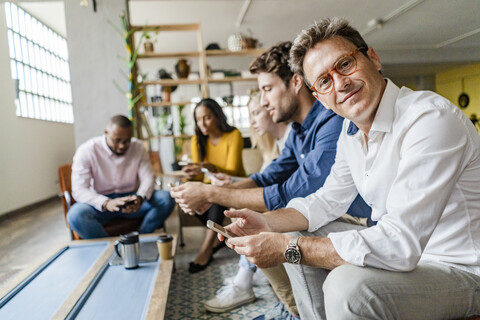 Geschäftsteam sitzt im Loft-Büro und benutzt Handys, lizenzfreies Stockfoto