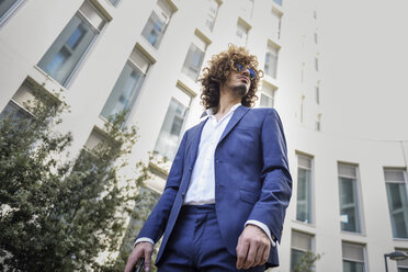 Junger modischer Geschäftsmann mit lockigem Haar in blauem Anzug und Sonnenbrille - JSMF00645