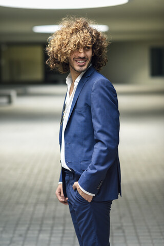 Porträt eines jungen, modischen Geschäftsmannes mit lockigem Haar und blauem Anzug, lizenzfreies Stockfoto