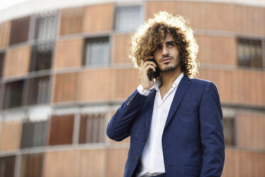 Portrait of young fashionable businessman with beard and curly hair on the phone - JSMF00669