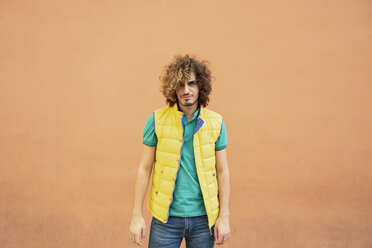 Portrait of annoyed young man with curly hair wearing yellow waistcoat outdoors - JSMF00675