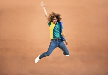 Fröhlicher junger Mann mit lockigem Haar und Weste, der in die Luft springt - JSMF00677
