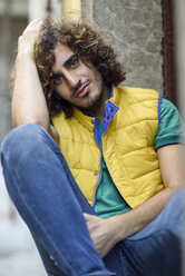 Portrait of smiling young man with beard and curly hair wearing yellow waistcoat - JSMF00689