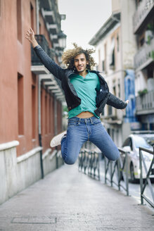 Porträt eines lächelnden jungen Mannes, der im Freien in die Luft springt - JSMF00693