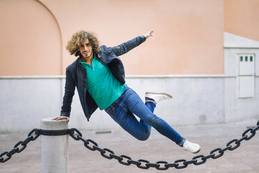 Portrait of smiling young man jumping over chain outdoors - JSMF00696