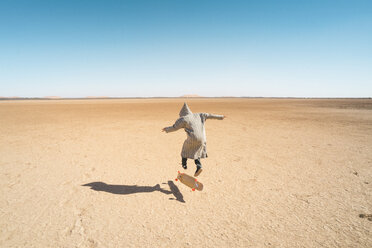 Rückansicht eines Mannes, der auf dem Sand Skateboard fährt, gegen einen klaren blauen Himmel - CAVF58296