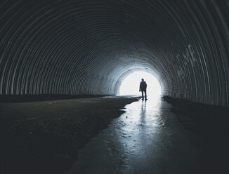 Rear view of silhouette boy standing in wet tunnel - CAVF58303