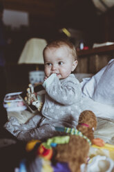 Cute baby girl biting her clothing while sitting on bed at home - CAVF58340