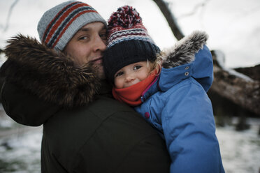 Porträt eines Vaters, der seine Tochter trägt, während er im Winter im Freien steht - CAVF58346