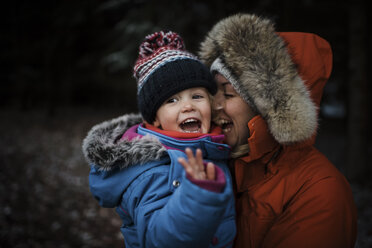 Glückliche Mutter, die ihre Tochter trägt, während sie im Winter im Wald steht - CAVF58348