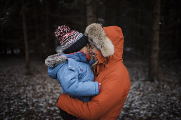 Happy mother carrying daughter while standing in forest during winter - CAVF58349