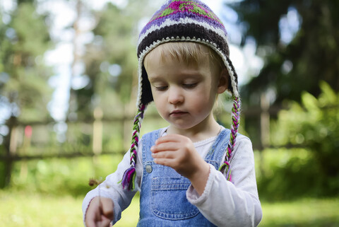 Porträt eines kleinen Mädchens mit gestrickter Mütze, das etwas in der Hand hält, lizenzfreies Stockfoto