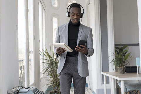 Portrait of young businessman with headphonbes and notebook in the office looking at cell phone stock photo