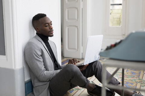 Portrait of young businessman sitting on the floor in the office working on laptop stock photo