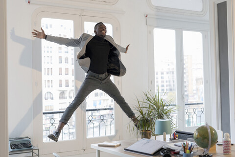 Glücklicher junger Geschäftsmann, der in seinem Büro in die Luft springt, lizenzfreies Stockfoto