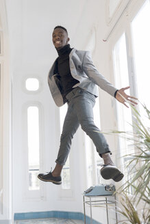 Porträt eines lächelnden jungen Geschäftsmannes, der in seinem Büro in die Luft springt - GRSF00026