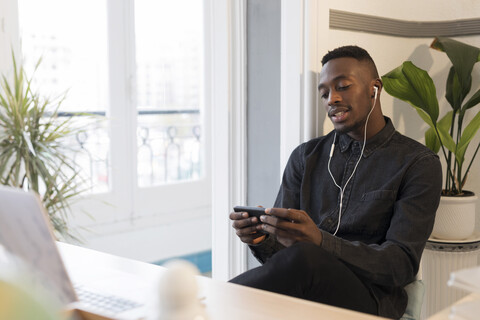 Porträt eines jungen Geschäftsmannes mit Smartphone und Kopfhörern im Büro, lizenzfreies Stockfoto